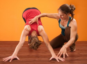 Yoga teacher helps student perform Adho Mukha Svanasana yoga posture